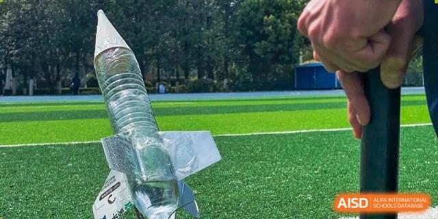 A water bottle rocket resting on the edge of a green sports field at the International Department of Kunming No.10 Middle School.