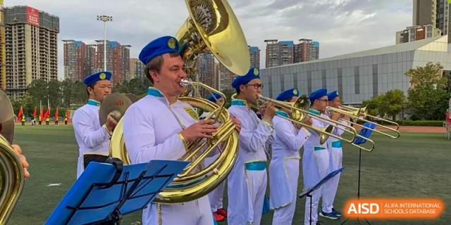 Brass band performance with a sousaphone player and trumpeters in white and blue uniforms for the International Department of Kunming No.10 Middle School.