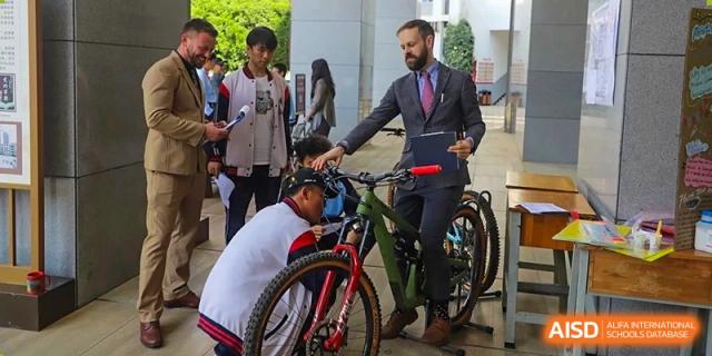 A man in a suit standing next to a mountain bike, talking with students at an event for the International Department of Kunming No.10 Middle School.