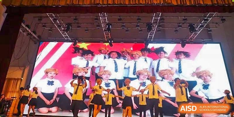A group of students in white uniforms and younger children in yellow costumes posing on a stage at the International Department of Kunming No.10 Middle School.