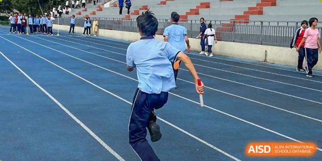 A student running with a baton on a blue track during a relay race at the International Department of Kunming No.10 Middle School.