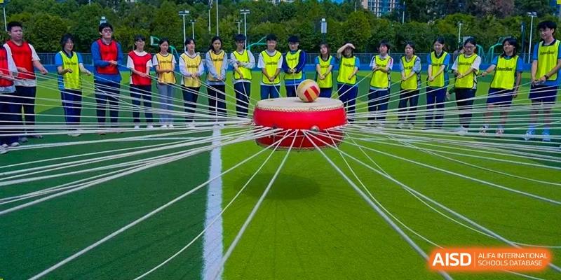 Students participating in a unique field game involving a large hoop and ropes at the International Department of Kunming No.10 Middle School.
