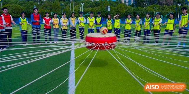 Students participating in a unique field game involving a large hoop and ropes at the International Department of Kunming No.10 Middle School.
