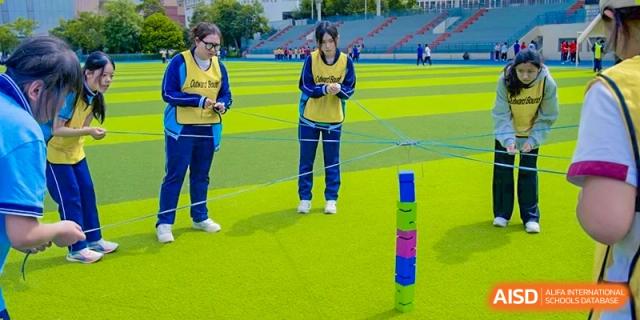 Students participating in a stacking or balancing game on the green field at the International Department of Kunming No.10 Middle School.
