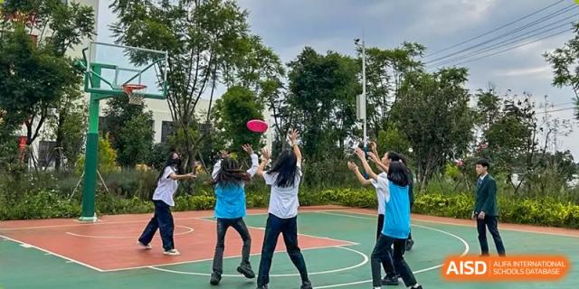 Two students from Kunming World Youth Academy jump to catch a frisbee on a sports field during a physical education class.
