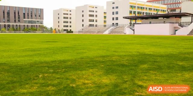A wide view of a grassy field and school buildings at Kunming World Youth Academy.