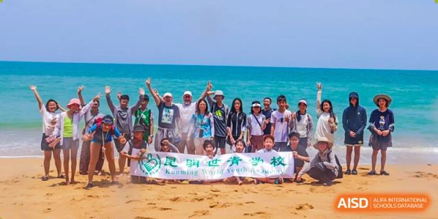 A group of students holding a banner and posing on a beach at Kunming World Youth Academy.