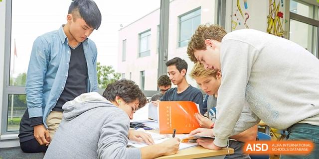 A group of Lycée Français de Shanghai students is gathered around a book and a tablet, studying together.