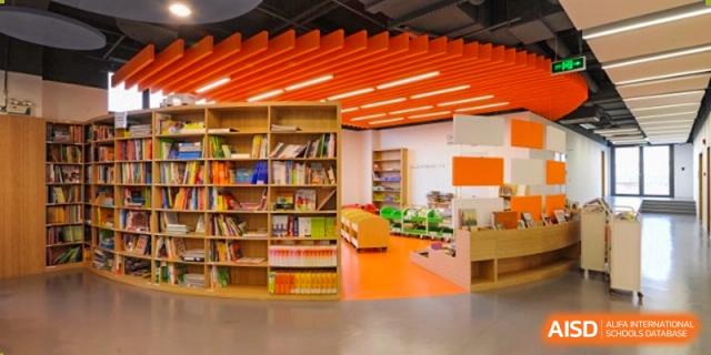 An indoor reading corner at Lycée Français de Shanghai is shown with orange accents, wooden bookshelves, and various books.