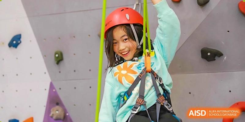 A female Lycée Français de Shanghai student wearing a helmet and climbing gear is smiling at the camera while on a climbing wall.