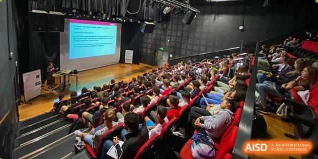 A large crowd of Lycée Français de Shanghai students is seated in an auditorium, attending an event.