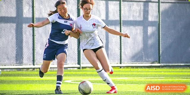 A female Lycée Français de Shanghai student is playing soccer and dribbling the ball on a field.