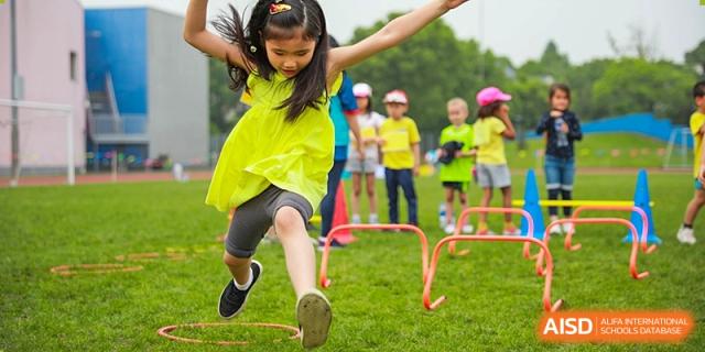 A female Lycée Français de Shanghai student is jumping over a hurdle on a green field.