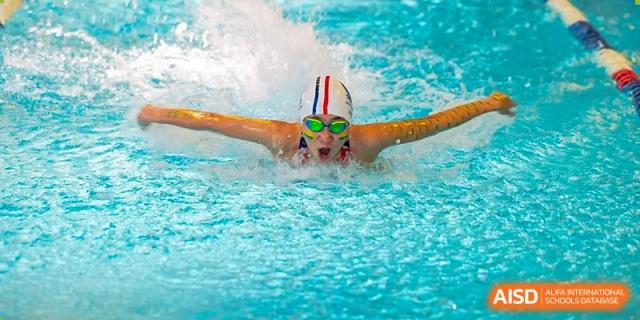 A female Lycée Français de Shanghai student wearing a swim cap and goggles is swimming in a pool.