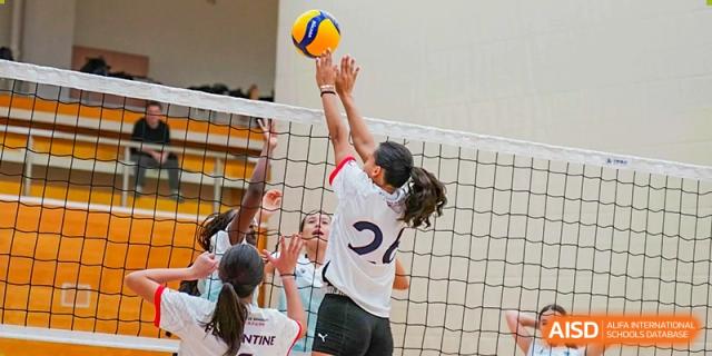 A female Lycée Français de Shanghai student is playing volleyball and jumping to hit the ball over the net.