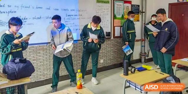 Students standing and working on tasks in a classroom or hallway, writing on clipboards at Maple Leaf School- Xiangyang.