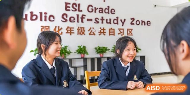 A smiling female student in a uniform sitting at a desk with an "ESL Grade Self-study Zone" sign visible behind her at Maple Leaf School- Xiangyang.