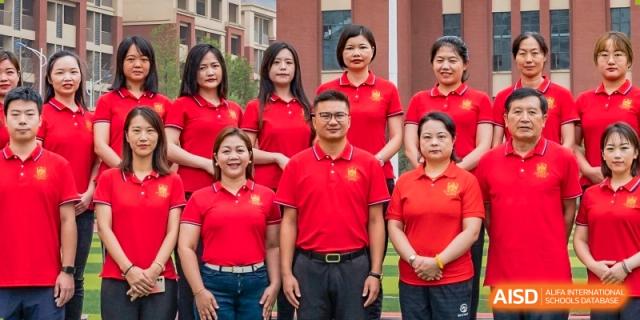 A group of female and male faculty members wearing matching red shirts posing together for a photo outside at Maple Leaf School- Xiangyang.