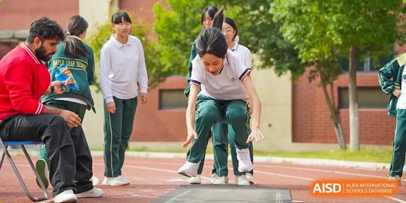 A female student from Maple Leaf School - Xiangyang landing in the long jump pit during a sports event.