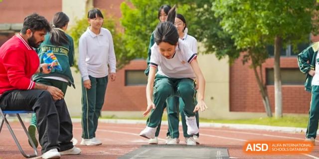 A female student from Maple Leaf School - Xiangyang landing in the long jump pit during a sports event.
