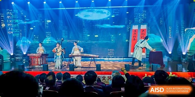 Students from Maple Leaf School - Xiangyang performing traditional Chinese music with instruments on a stage in front of an audience.
