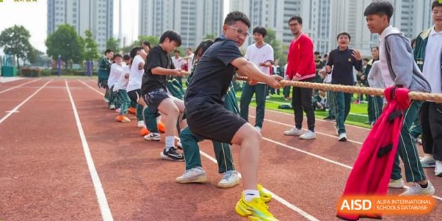 A group of adults from Maple Leaf School - Xiangyang participating in a competitive tug-of-war game on a track.