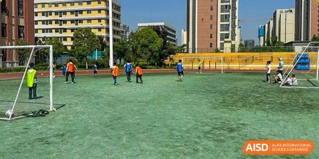 Students from Maple Leaf School - Xiangyang playing soccer or participating in a sports activity on a green turf field.