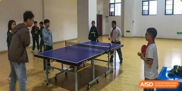 Two people, possibly students or staff from Maple Leaf School - Xiangyang, playing table tennis (ping pong) in an indoor area.