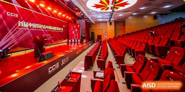 The interior of an auditorium or large hall at Maple Leaf School - Xiangyang, set up for an event with red seating and stage lighting.