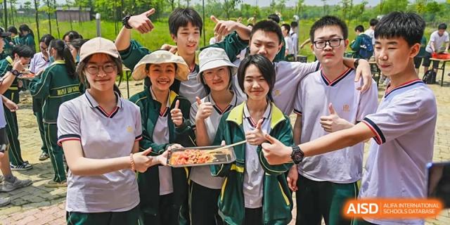 A group of happy students outdoors, holding food skewers and giving thumbs up, participating in a health or nutrition event at Maple Leaf School- Xiangyang.