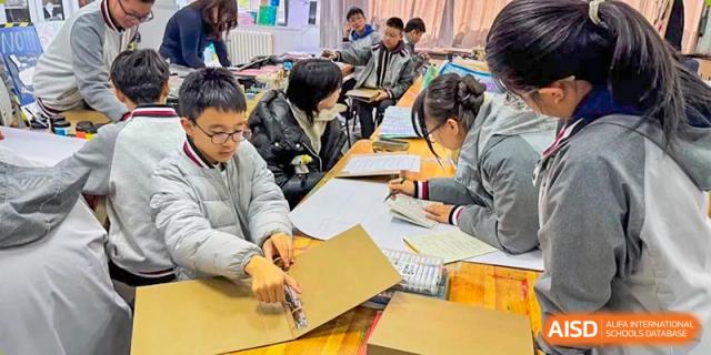 Students working together on a collaborative project, measuring and cutting cardboard in a classroom at Weiming International Qingdao.