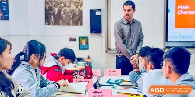 A male teacher standing and supervising students as they work at their desks in a classroom setting at Weiming International Qingdao.