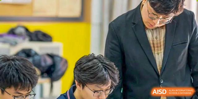 A close-up of a male student wearing glasses, looking down and focused on his work during a class at Weiming International Qingdao.
