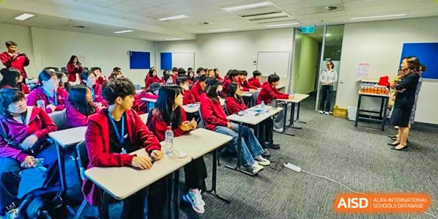 A large class of students wearing red jackets, seated at individual desks during a lesson in a brightly lit classroom at Weiming International Qingdao.