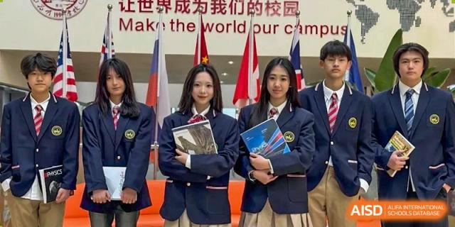 Two female students in school uniform holding books and posing in front of a backdrop featuring various flags at Weiming International Qingdao.