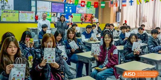 Students in a classroom, some holding small signs or books, smiling towards the camera with international flags visible at Weiming International Qingdao.