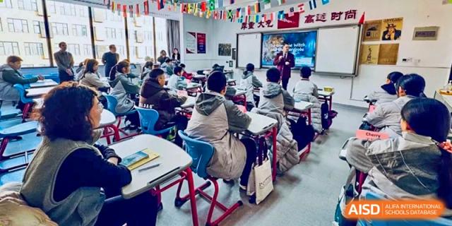 A teacher standing in front of the class, lecturing or presenting to students seated at their desks in a classroom setting at Weiming International Qingdao.