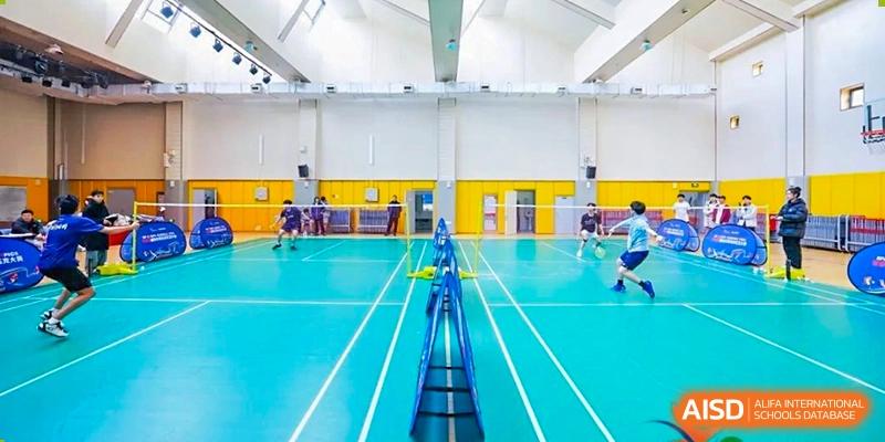 Students playing badminton on the indoor sports court at Weiming International Qingdao. The bright blue and yellow court markings are clearly visible.