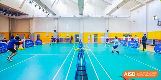Students playing badminton on the indoor sports court at Weiming International Qingdao. The bright blue and yellow court markings are clearly visible.