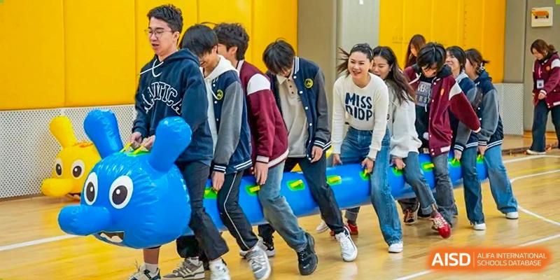 Students participating in an indoor relay or game involving blue cylindrical props at Weiming International Qingdao.