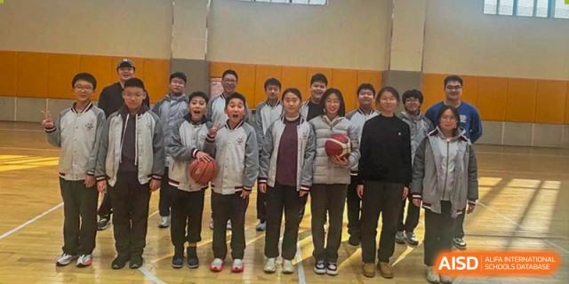 A group of male and female students posing indoors with basketballs, possibly a sports team, at Weiming International Qingdao.