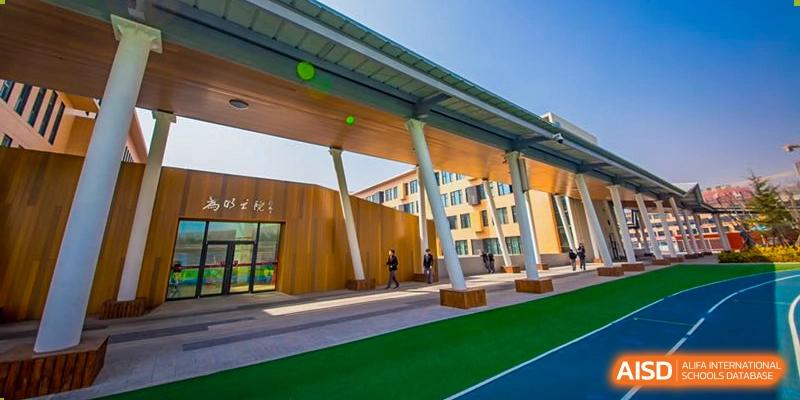 A low-angle view of a modern school building with covered outdoor corridors and green artificial turf at Weiming International Qingdao.