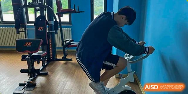 A student exercising on a stationary bike or similar fitness equipment in the school gym or fitness center at Weiming International Qingdao.