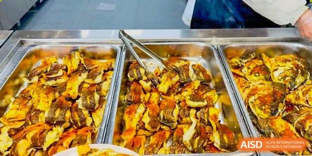 A serving tray filled with a cooked main dish, possibly seafood or poultry with vegetables, available at the school cafeteria at Weiming International Qingdao.