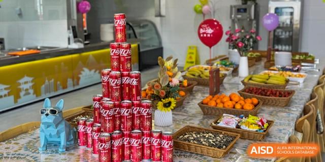 A display of food and beverages including a pyramid of Coca-Cola cans, fruits, and snacks at an event at Weiming International Qingdao.