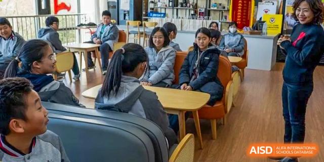 Students seated around a small round table, talking or studying together in a brightly lit common area at Weiming International Qingdao.