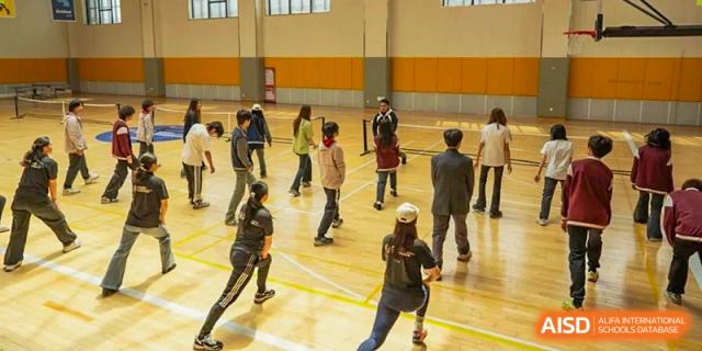 A group of students participating in an indoor physical education or fitness class, exercising on a large wooden floor at Weiming International Qingdao.