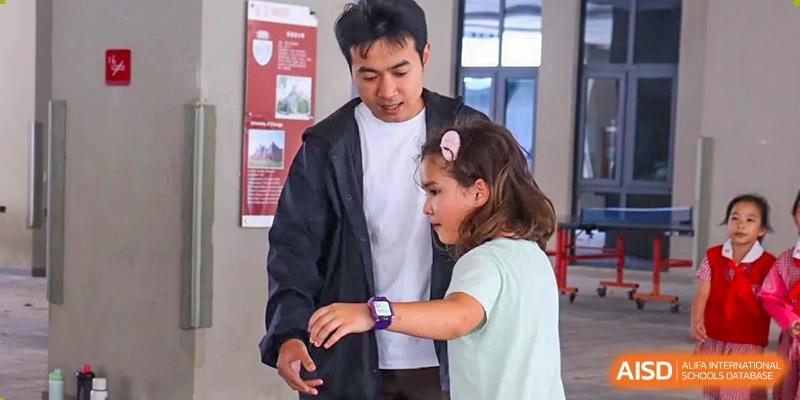 A teacher from Sanya Haiya  Foreign Language School helps a young student check her smartwatch.