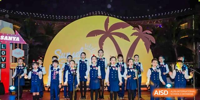 The Sanya Haiya  Foreign Language School choir performing on a stage with palm tree decorations.