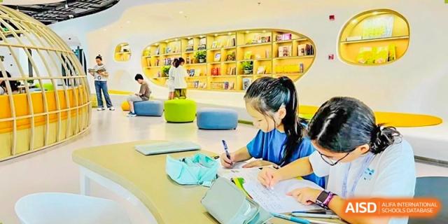 A young female student writing at a desk in a bright, modern library area at Shanghai High School International Division.